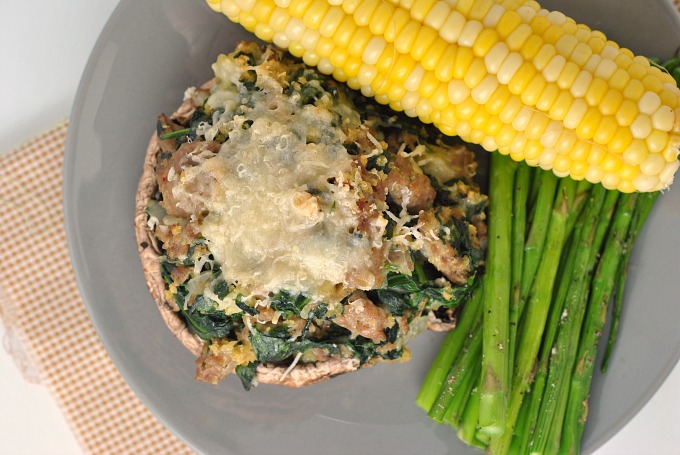 Top-down image of a stuffed mushroom covered in cheese with sides of corn on the cob and asparagus. 