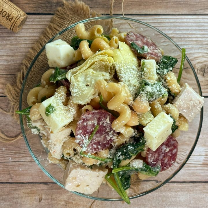 High protein Italian pasta salad with chicken, salami, mozzarella, spinach, and artichokes in a glass bowl