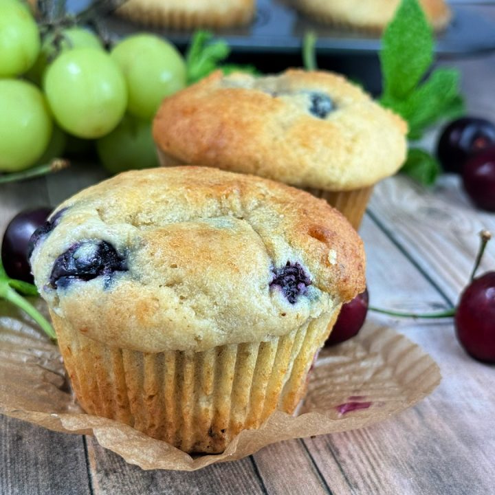 Blueberry cottage cheese muffins made with whole wheat flour and fresh blueberries, baked until golden brown and served on a rustic wooden table with fresh fruit. A healthy, high-protein breakfast muffin recipe