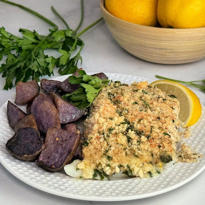 Herb-crusted cod fillet with a crispy parsley and Parmesan breadcrumb topping, served with roasted purple potatoes and lemon wedges